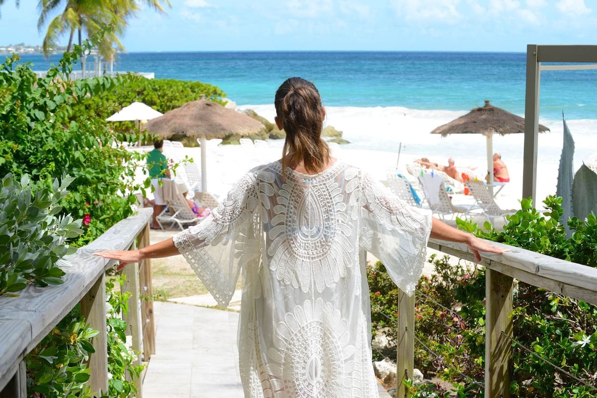 A guest walking towards a pristine beach, surrounded by tropical plants and shaded pathways leading to the sea.