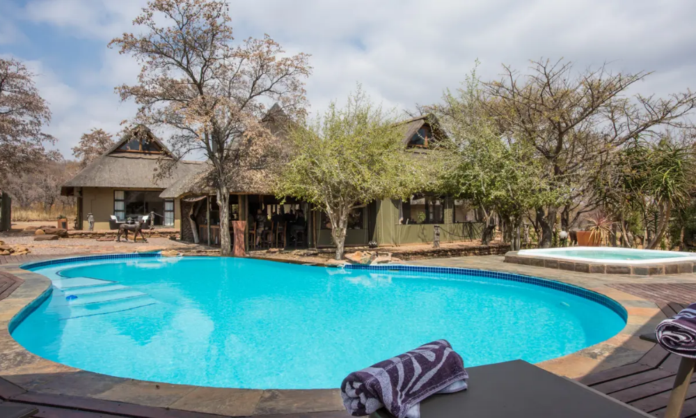 Outdoor swimming pool and jacuzzi at Elephant Lodge, with the lodge's buildings and lush trees in the background.