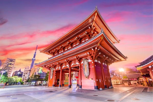 The iconic Senso-ji Temple in Tokyo, Japan, illuminated at sunset with a vibrant pink and orange sky in the background.